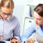 Two accountants at a desk calculating numbers and reviewing financial documents.