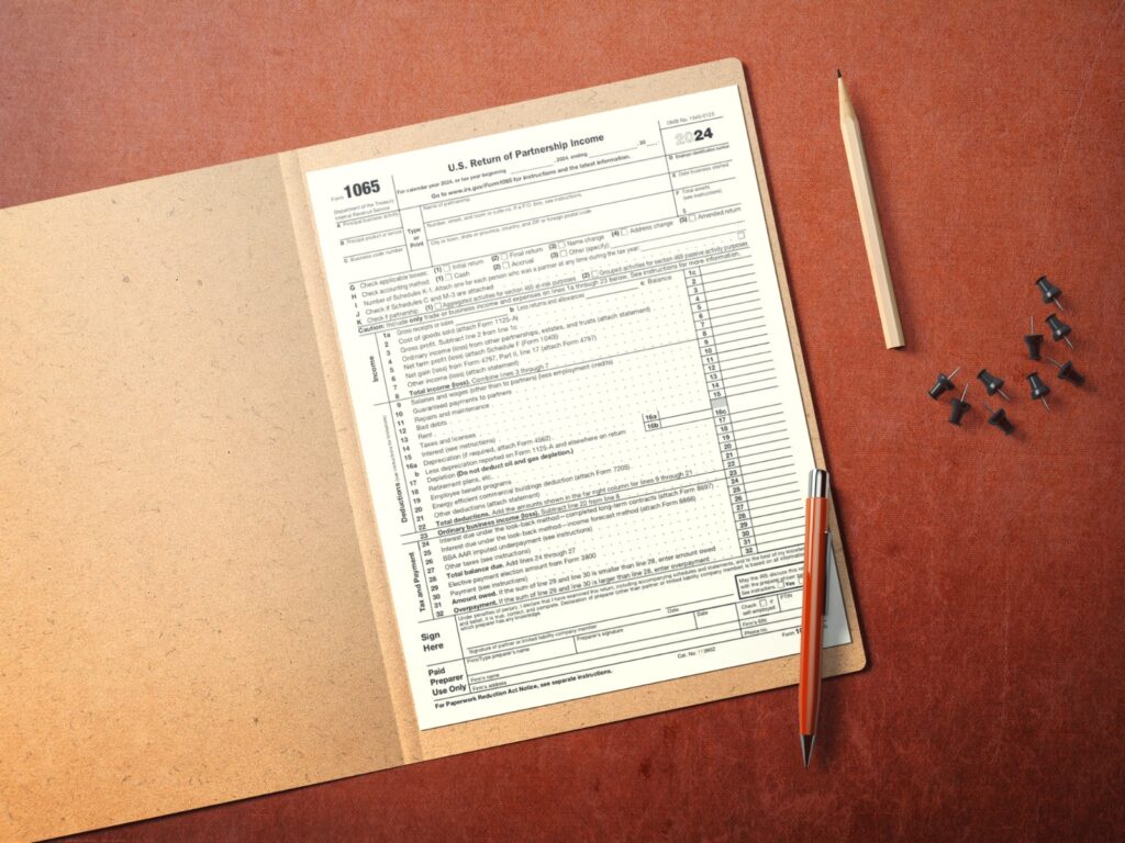 IRS Form 1065, U.S. Return of Partnership Income, placed on a clipboard with a pencil and pen, representing tax filing requirements for partnerships.