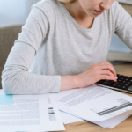 A woman calculates her taxes using a calculator, focused on her financial task.