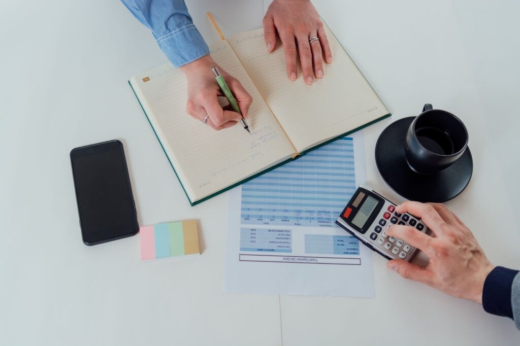 Two people reviewing financial documents and using a calculator while discussing payroll tax details.