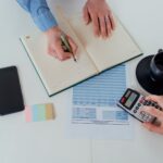 Two people reviewing financial documents and using a calculator while discussing payroll tax details.