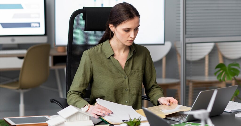 A woman at a desk with a laptop and papers, focused on bookkeeping for small businesses.