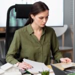 A woman at a desk with a laptop and papers, focused on bookkeeping for small businesses.