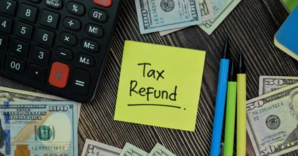 Calculator, cash, and a "Tax Refund" sticky note on a wooden desk.