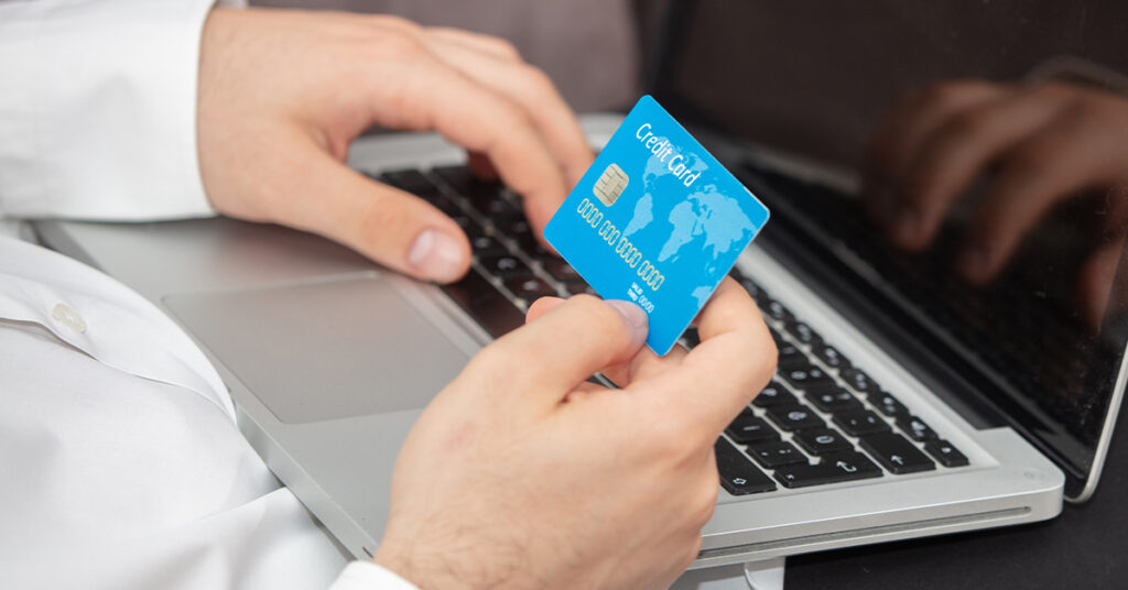 A close-up of a person holding a blue credit card while typing on a laptop keyboard.