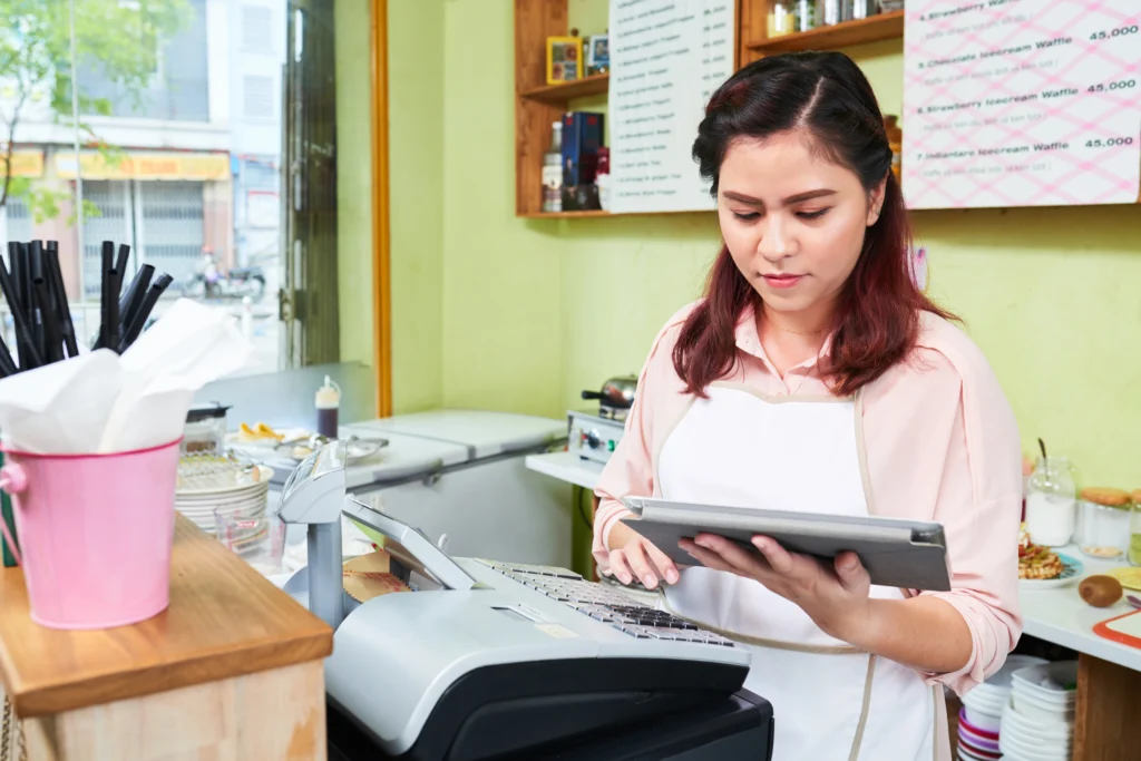 Female store clerk using a digital tablet at a cash register.