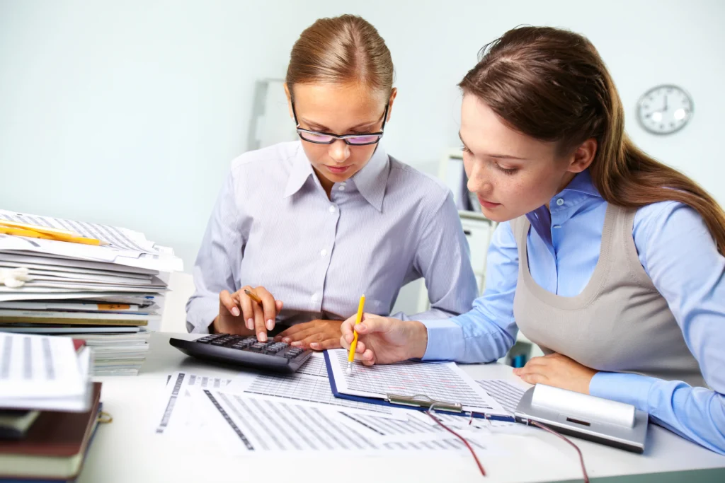 Two accountants at a desk calculating numbers and reviewing financial documents.
