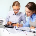 Two accountants at a desk calculating numbers and reviewing financial documents.